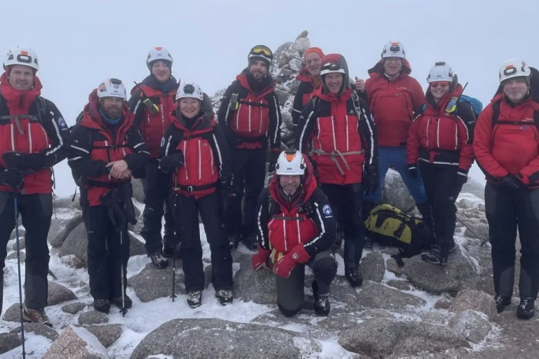 A group of people in red coat pose for a picture on top of a snow covered mountain 