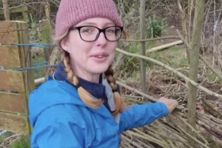 A woman knelt down fixing a woodland fence.