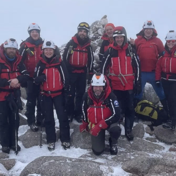 A group of people in red coat pose for a picture on top of a snow covered mountain 